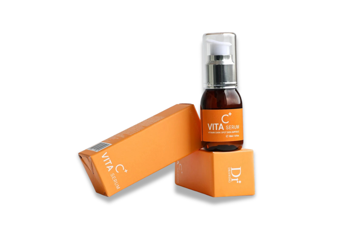 A small amber glass serum bottle with a clear cap stands on top of an orange box, with a second orange box leaning beside it on a white background. The bottle label reads VITA SERUM, and the box shows Dr.
