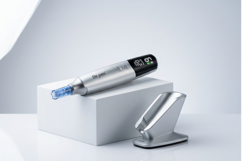 A silver and black Depen pen device with a blue tip rests on a white display block, with its matching metallic charging dock beside it on a clean light gray studio background.