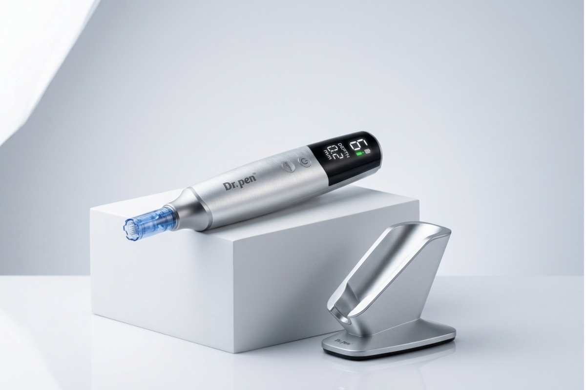 A silver and black Depen pen device with a blue tip rests on a white display block, with its matching metallic charging dock beside it on a clean light gray studio background.
