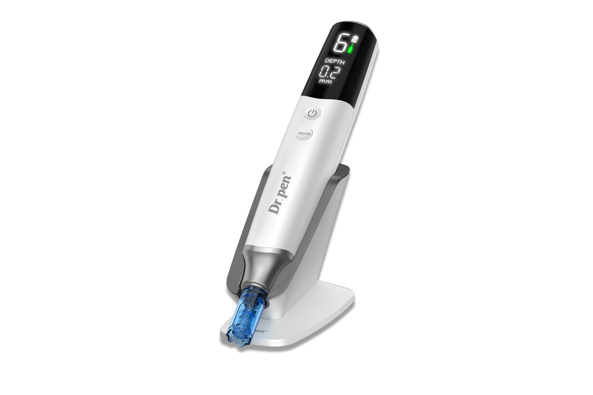 A white and silver Dr. Pen tattoo pen with a digital display screen on the top, resting on its matching white charging stand against a solid white background.