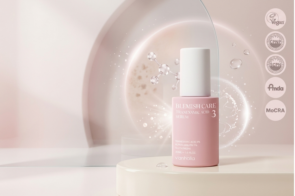 A pink bottle of Blemish Care Transamin Acid Serum by Gholia stands on a white pedestal against a soft, abstract pink background with water droplets and circular certification badges on the right.